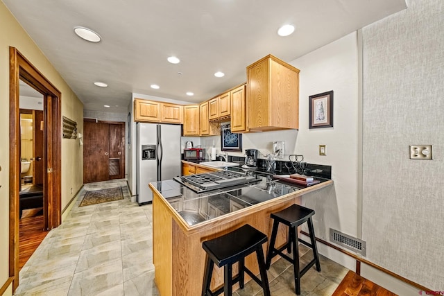 kitchen featuring kitchen peninsula, appliances with stainless steel finishes, light brown cabinetry, a kitchen breakfast bar, and sink