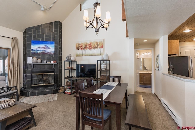 dining room with a tile fireplace, an inviting chandelier, a baseboard heating unit, vaulted ceiling, and light carpet