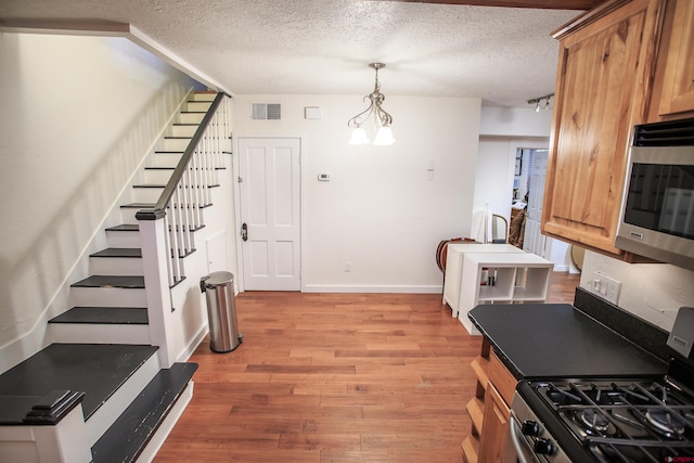 kitchen featuring a textured ceiling, stainless steel appliances, decorative light fixtures, light hardwood / wood-style flooring, and a chandelier