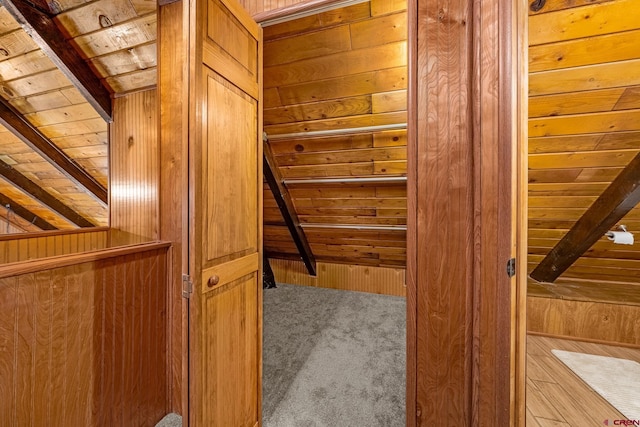 interior space featuring carpet flooring, wooden walls, wood ceiling, and beam ceiling