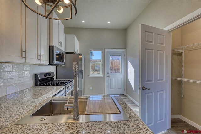 kitchen featuring light stone countertops, white cabinetry, stainless steel appliances, a chandelier, and decorative backsplash