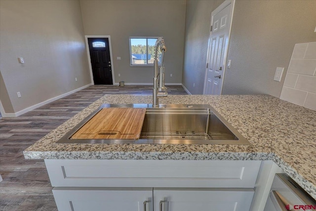 kitchen with light stone countertops, white cabinetry, dark wood-type flooring, and sink