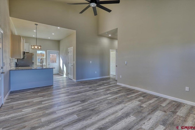 unfurnished living room with a towering ceiling, light hardwood / wood-style floors, ceiling fan, and sink