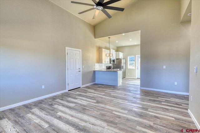 unfurnished living room featuring light wood-type flooring, high vaulted ceiling, and ceiling fan