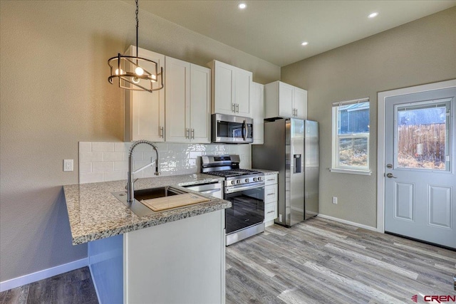 kitchen featuring pendant lighting, backsplash, white cabinets, kitchen peninsula, and stainless steel appliances