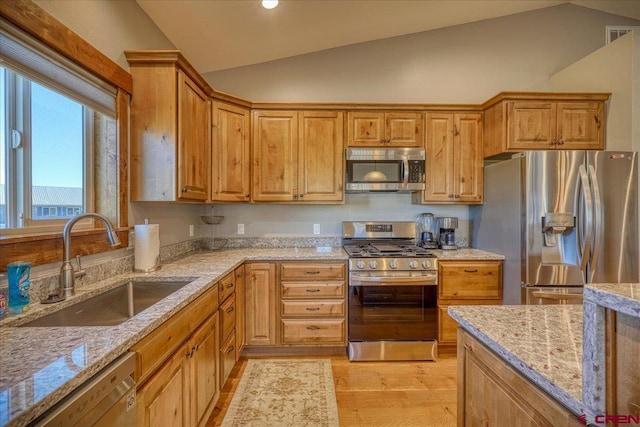 kitchen with appliances with stainless steel finishes, light stone counters, lofted ceiling, and sink