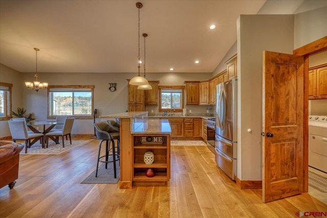 kitchen with a center island, vaulted ceiling, appliances with stainless steel finishes, a kitchen bar, and washer / dryer