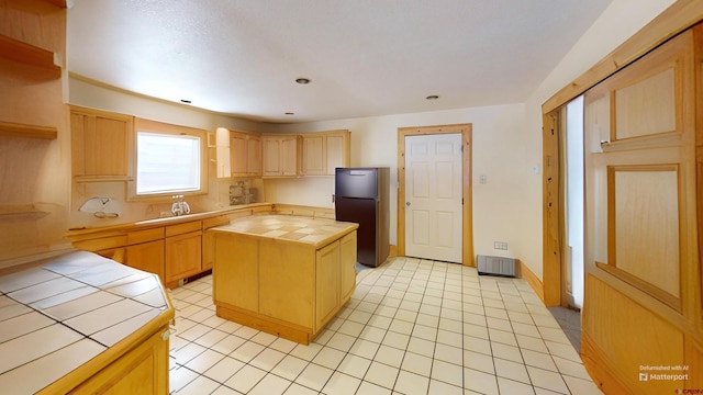 kitchen with tile counters, a center island, refrigerator, and light brown cabinets