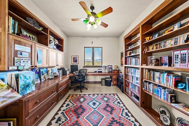 office space with light carpet, ceiling fan, built in desk, and a textured ceiling