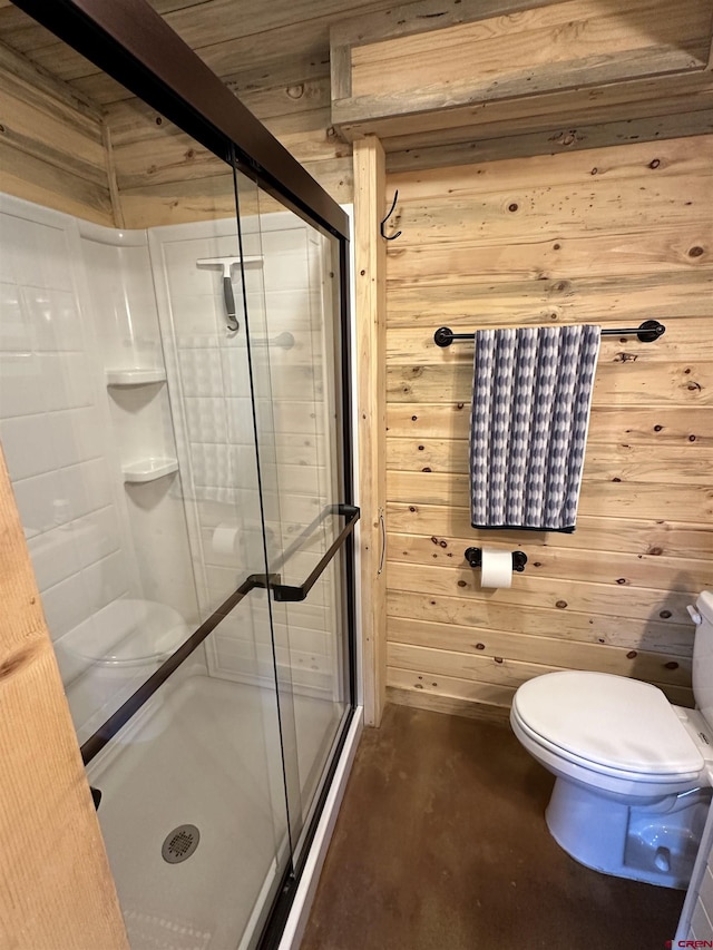 bathroom featuring concrete flooring, a shower with door, beam ceiling, toilet, and wood walls