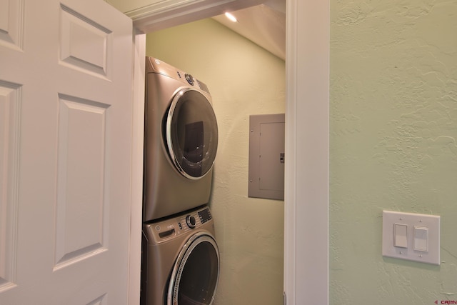 clothes washing area with electric panel and stacked washer and clothes dryer