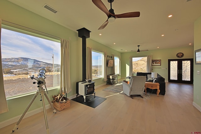 living room with a mountain view, a wood stove, french doors, ceiling fan, and light wood-type flooring