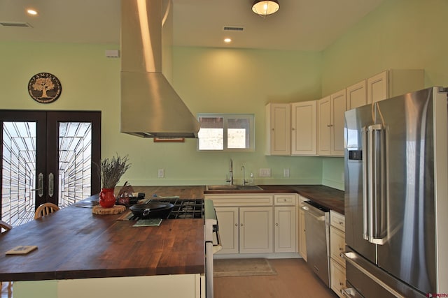 kitchen with butcher block counters, french doors, sink, ventilation hood, and appliances with stainless steel finishes