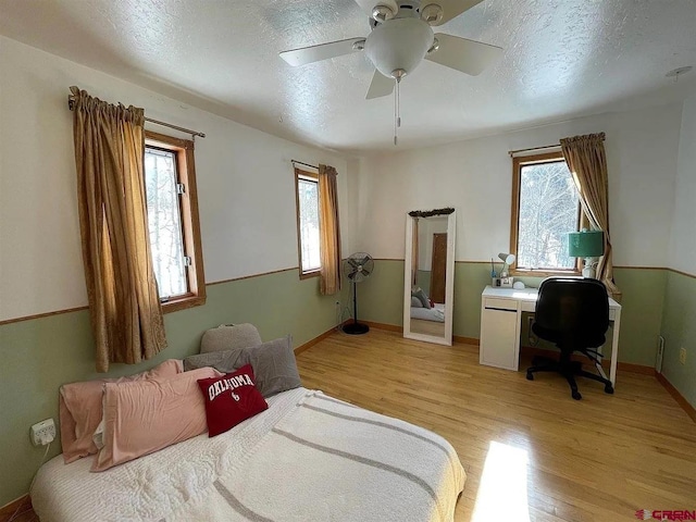 bedroom featuring ceiling fan, a textured ceiling, multiple windows, and light hardwood / wood-style floors