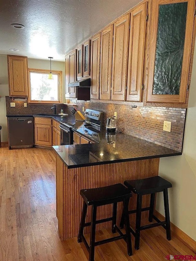 kitchen featuring kitchen peninsula, electric range, black dishwasher, light hardwood / wood-style flooring, and a breakfast bar area