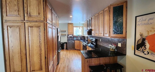 kitchen with tasteful backsplash, kitchen peninsula, light hardwood / wood-style flooring, a kitchen breakfast bar, and stainless steel appliances