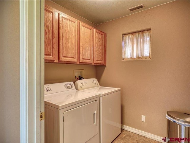 clothes washing area featuring washer and dryer, light tile patterned flooring, and cabinets