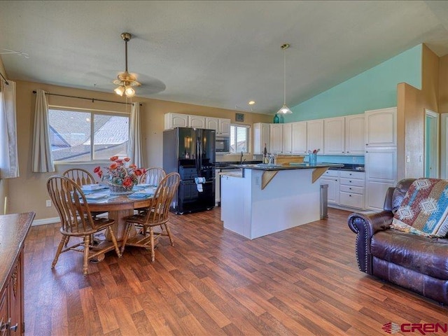 kitchen with black fridge, dark wood-type flooring, white cabinetry, a kitchen island, and a breakfast bar area