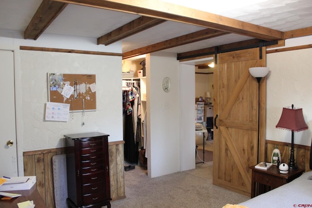 carpeted bedroom with beam ceiling, a barn door, a walk in closet, and wooden walls