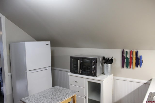 kitchen featuring white refrigerator, white cabinetry, and vaulted ceiling