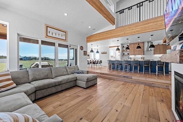 living room featuring beamed ceiling, light hardwood / wood-style floors, high vaulted ceiling, and sink