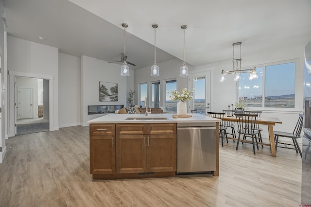 kitchen featuring a kitchen island with sink, sink, stainless steel dishwasher, light wood-type flooring, and decorative light fixtures