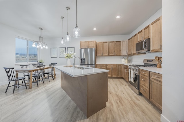 kitchen featuring stainless steel appliances, sink, decorative light fixtures, light hardwood / wood-style flooring, and an island with sink