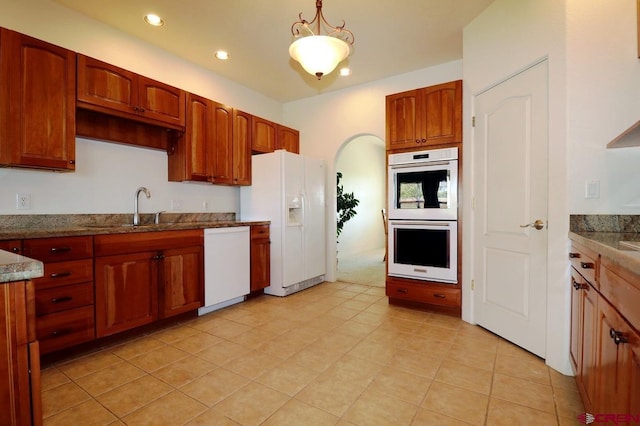 kitchen featuring sink, hanging light fixtures, dark stone counters, white appliances, and light tile patterned floors