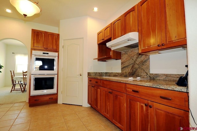 kitchen with decorative backsplash, light stone countertops, double wall oven, stovetop, and light tile patterned flooring