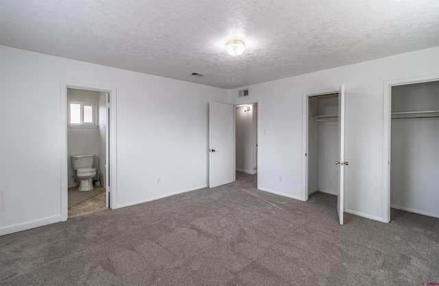 unfurnished bedroom with two closets, connected bathroom, carpet floors, and a textured ceiling