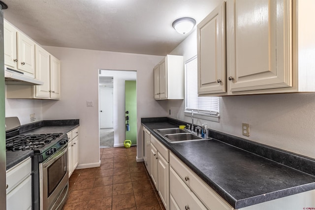 kitchen featuring gas stove, white cabinetry, dark tile patterned floors, and sink