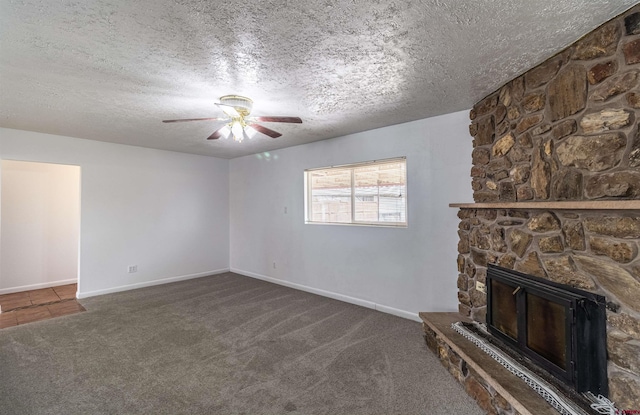 unfurnished living room featuring ceiling fan, dark carpet, a stone fireplace, and a textured ceiling