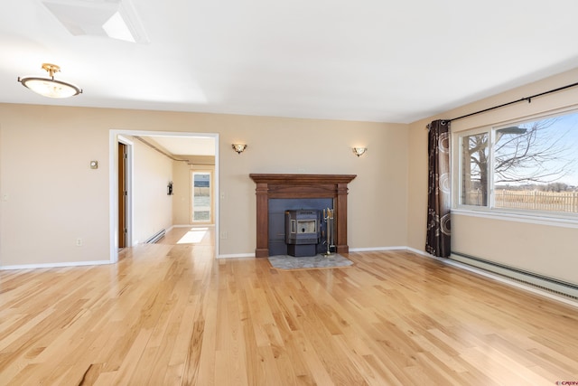 unfurnished living room with light wood-type flooring, a wood stove, and a baseboard radiator