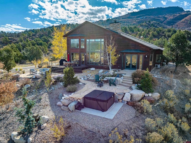 rear view of property featuring a hot tub, french doors, a deck with mountain view, and a patio area