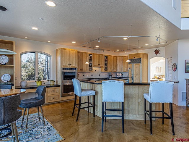 kitchen featuring a breakfast bar area, double oven, tasteful backsplash, and paneled built in fridge