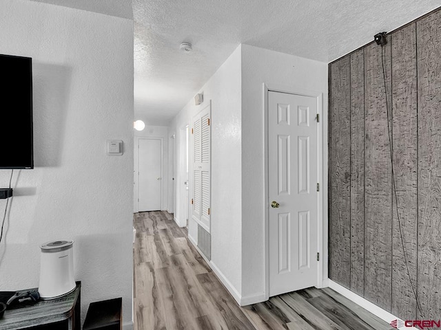 hall with a textured ceiling, light hardwood / wood-style floors, and wood walls