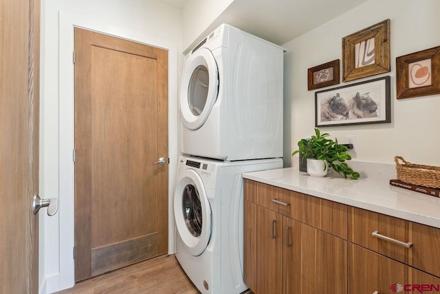 laundry room with light wood finished floors, cabinet space, and stacked washer and clothes dryer