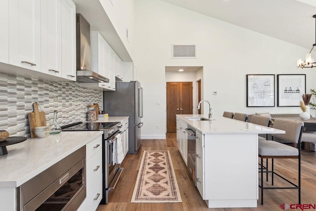 kitchen featuring wood finished floors, visible vents, a kitchen breakfast bar, wall chimney range hood, and appliances with stainless steel finishes