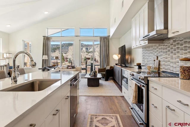 kitchen featuring stainless steel appliances, white cabinets, vaulted ceiling, a sink, and wall chimney range hood