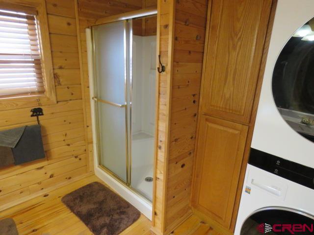 bathroom featuring a shower with door, stacked washer / drying machine, and wooden walls