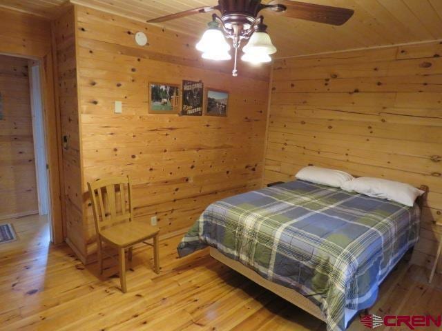 bedroom with hardwood / wood-style flooring, ceiling fan, and wooden walls