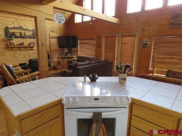 kitchen with tile countertops, light brown cabinetry, white electric stove, and wooden walls