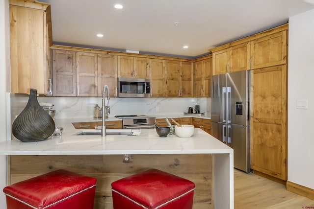 kitchen featuring sink, a breakfast bar area, appliances with stainless steel finishes, backsplash, and kitchen peninsula