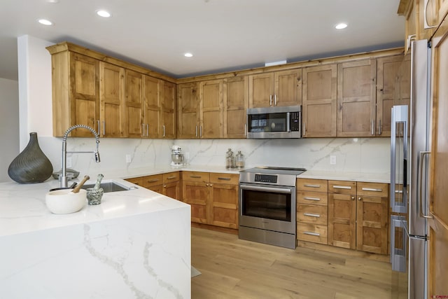 kitchen featuring appliances with stainless steel finishes, tasteful backsplash, sink, light stone counters, and light hardwood / wood-style flooring