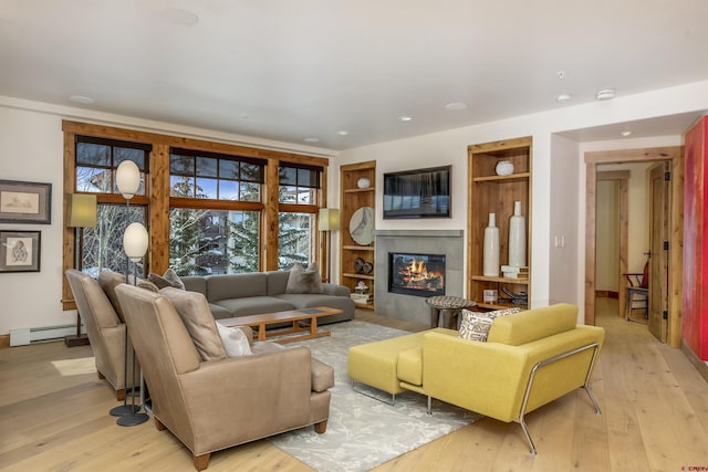 living room featuring baseboard heating, a tiled fireplace, light hardwood / wood-style floors, and built in shelves