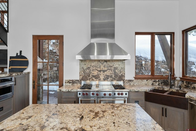 kitchen featuring light stone counters, sink, stainless steel appliances, and wall chimney range hood