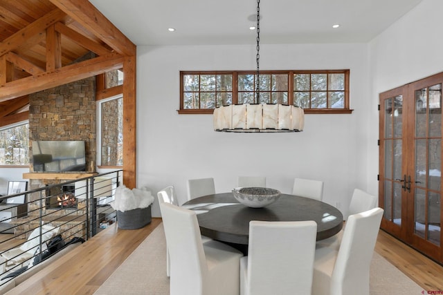 dining space featuring vaulted ceiling with beams, a stone fireplace, light wood-type flooring, and french doors