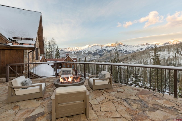 snow covered back of property with a patio area, a mountain view, and an outdoor living space with a fire pit