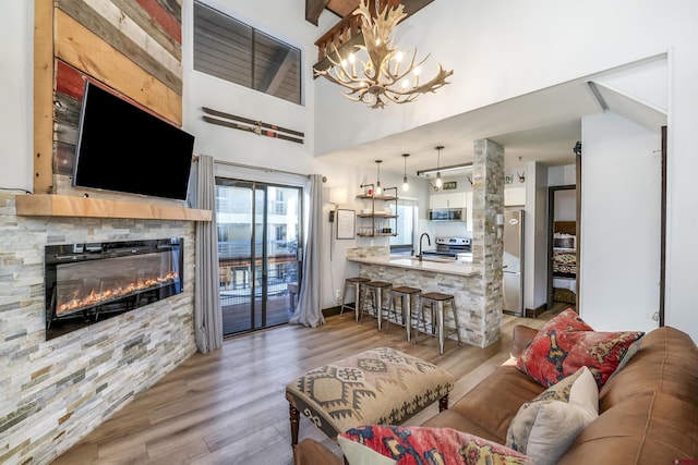 living room with sink, an inviting chandelier, a stone fireplace, light hardwood / wood-style flooring, and a towering ceiling