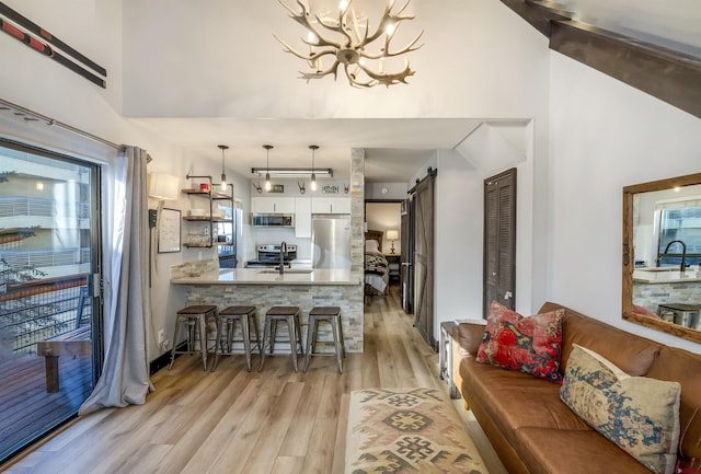 living room featuring a barn door, sink, light hardwood / wood-style flooring, and an inviting chandelier